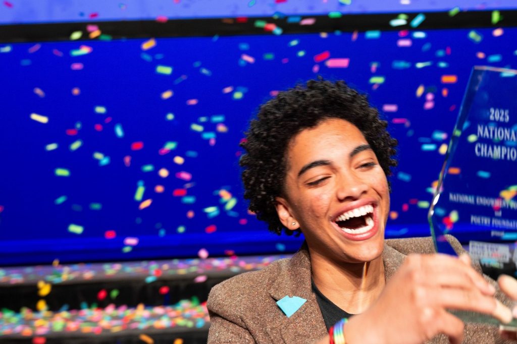 A student celebrates as confetti falls, He holds a trophy and smiles.
